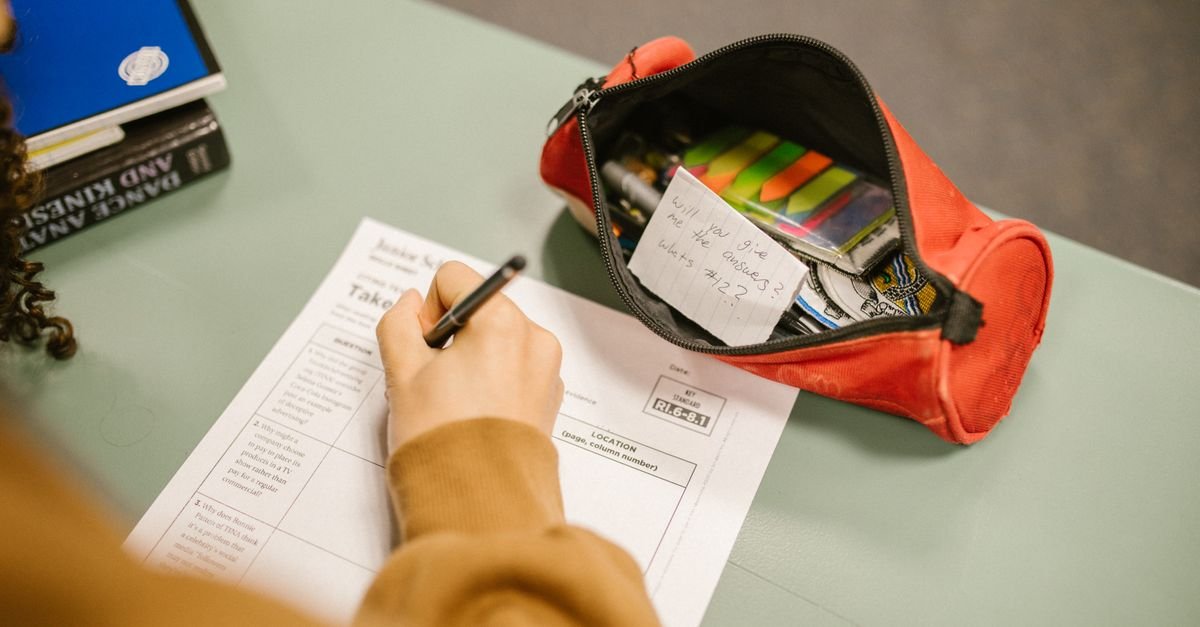 Tutor marking a mock exam paper with exam kit stationery on the desk